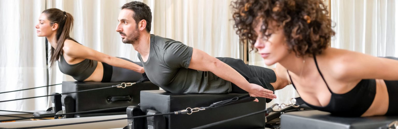 Male and female athletes in activewear doing thoracic extension exercise on box on reformer during pilates training in gym