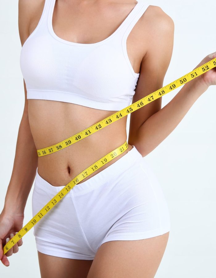 Close up slimming female with beautiful body and measuring her waistline  with measure tape on white background and copy space